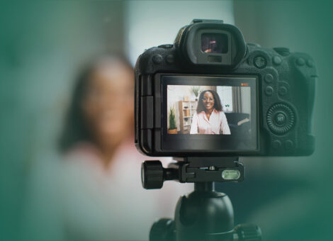 woman talking and gesturing in front of modern video camera while sitting on blur background